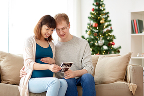 pregnancy, winter holidays and people concept - happy husband and his pregnant wife with baby ultrasound images home at christmas