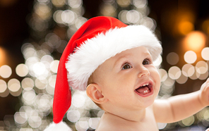 christmas, holidays and people concept - close up of happy little baby boy or girl in santa hat over lights background