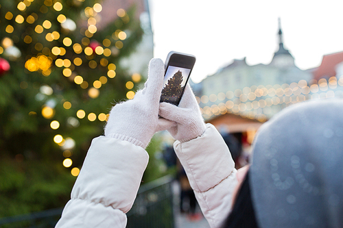 holidays, technology and people concept - hands with smartphone photographing christmas tree at old town hall square in tallinn