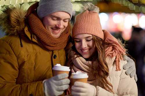 winter holidays, hot drinks and people concept - happy young couple with coffee over christmas lights in evening
