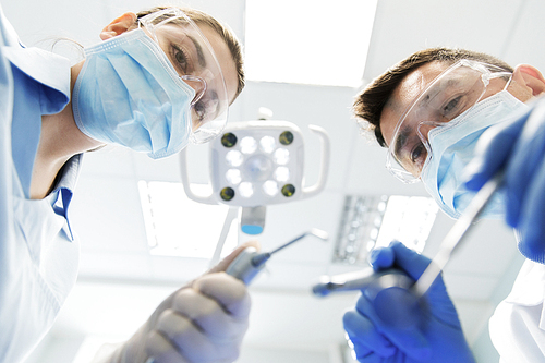 people, medicine, stomatology and health care concept - close up of dentist and assistant with dental mirror, drill and air water gun spray treating patient teeth at dental clinic