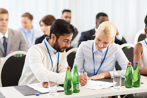 business, people and education concept - businessman and businesswoman at international conference discussing papers