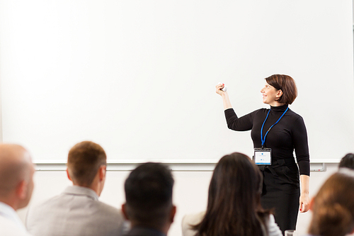 business, education and people concept - smiling businesswoman or teacher with remote and group of students at conference presentation or lecture