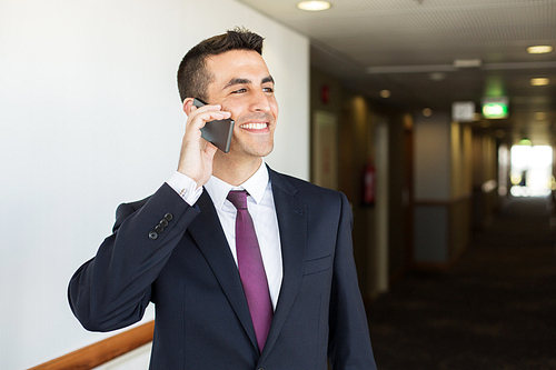 business trip, people and communication concept - happy smiling businessman calling on smartphone at hotel corridor