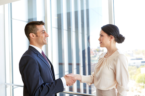 business, partnership and people concept - smiling man and woman shaking hands at office
