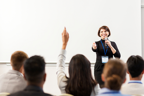 business, education and people concept - smiling businesswoman or teacher with microphone answering questions at conference presentation or lecture