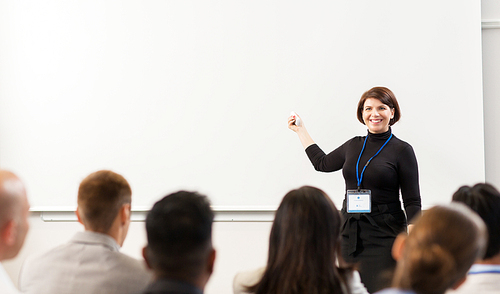 business, education and people concept - smiling businesswoman or teacher with remote and group of students at conference presentation or lecture