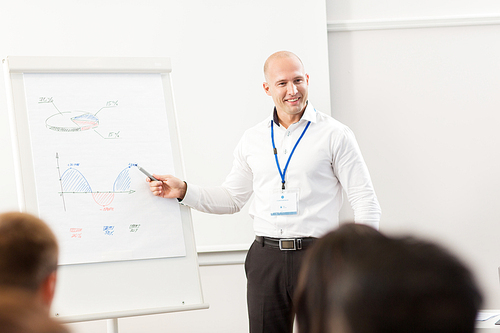 business, education and strategy concept - smiling businessman showing charts on whiteboard to group of people at conference presentation