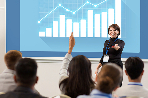 business, statistics and people concept - smiling businesswoman or lecturer with diagram chart on projection screen answering questions at conference presentation or lecture