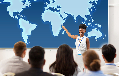 business, education and people concept - smiling african american businesswoman or lecturer showing world map on projection screen to group of students at conference presentation or lecture