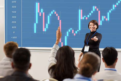 business, economy and people concept - smiling businesswoman or financier with forex chart on projection screen answering questions at conference presentation or lecture