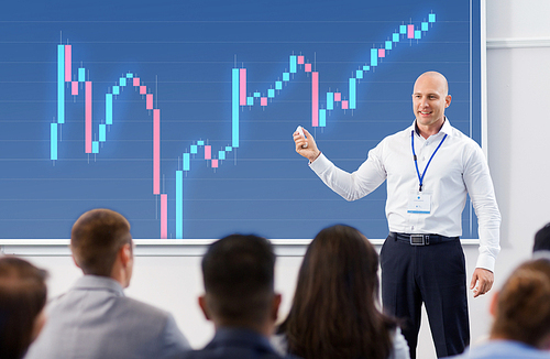 business, economy and people concept - smiling businessman or financier with forex chart on projection screen and group of students at conference presentation or lecture