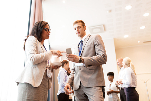 business, technology, people and education concept - happy couple with smartphone at international conference