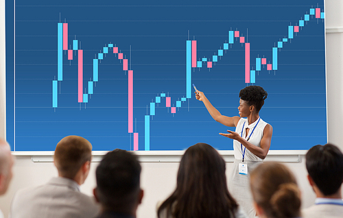 business, economy and people concept - smiling african american businesswoman or financier showing forex chart on projection screen to group of students at conference presentation or lecture