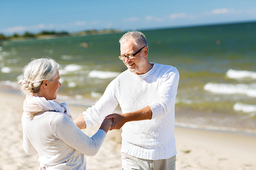 family, age, travel, tourism and people concept - happy senior couple holding hands and dancing on summer beach