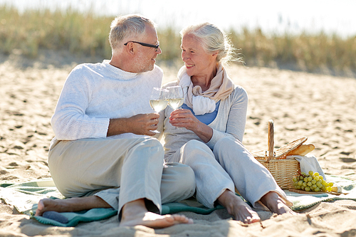 family, age, holidays, leisure and people concept - happy senior couple having picnic and clinking wine glasses on summer beach