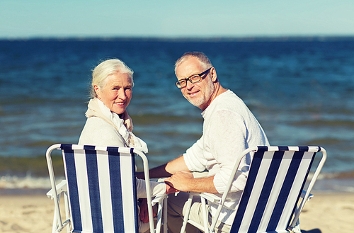 family, age, travel, tourism and people concept - happy senior couple sitting on deck chairs on summer beach