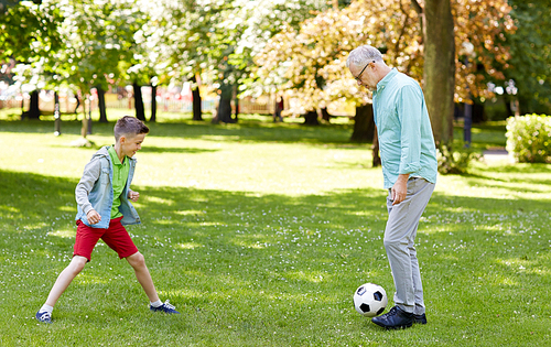 family, generation, game, sport and people concept - happy grandfather and grandson playing football at summer park