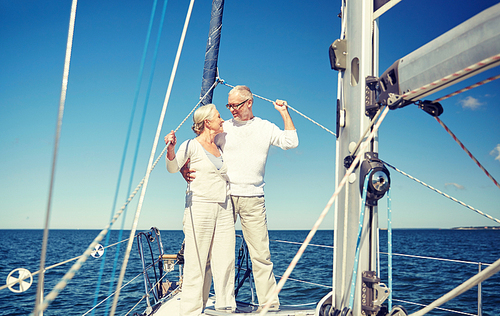 sailing, age, tourism, travel and people concept - happy senior couple hugging and talking on sail boat or yacht deck floating in sea