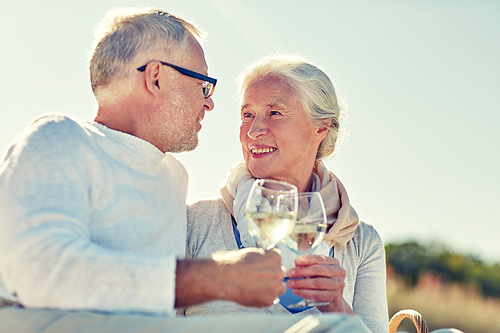 family, age, holidays, leisure and people concept - happy senior couple having picnic and clinking wine glasses on summer beach