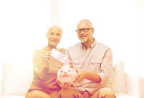 family, savings, age and people concept - smiling senior couple with money and piggy bank at home