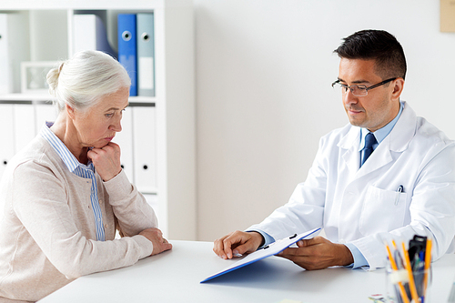 medicine, age, healthcare and people concept - senior woman and doctor with clipboard meeting at hospital