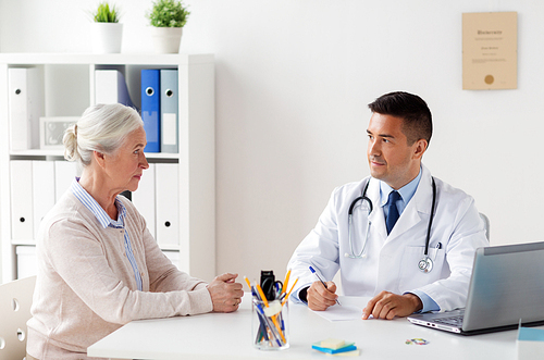 medicine, age, healthcare and people concept - senior woman and doctor with laptop computer writing prescription at hospital