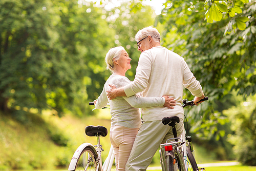 old age, people and lifestyle concept - happy senior couple with bicycles hugging at summer city park