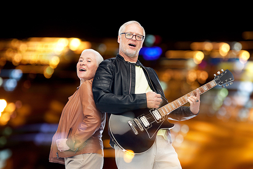 music, age and people concept - happy senior couple with electric guitar singing over night lights background