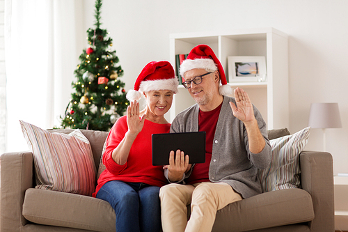 christmas, holidays, communication and people concept - happy smiling senior couple in santa hats with tablet pc computer having video chat at home