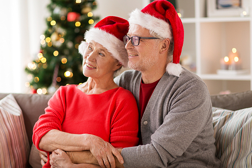 christmas, holidays and people concept - happy smiling senior couple in santa hats at home