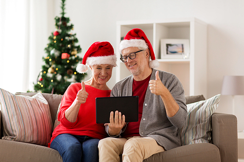 christmas, holidays, communication and people concept - happy smiling senior couple in santa hats with tablet pc computer having video chat at home