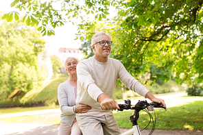 old age, people and lifestyle concept - happy senior couple riding together on bicycle at summer city park