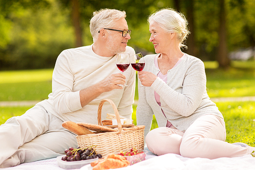 old age, holidays, leisure and people concept - happy senior couple with picnic basket and wine glasses sitting on blanket at summer park