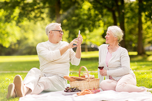 old age, leisure and people concept - happy senior couple with picnic basket and wine taking picture by smartphone at summer park