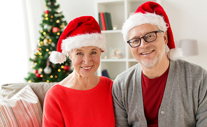 christmas, holidays and people concept - happy smiling senior couple in santa hats at home