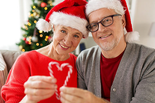 christmas, holidays and people concept - close up of happy smiling senior couple in santa hats with candy canes at home