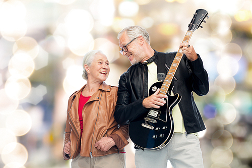 music, age and people concept - happy senior couple with electric guitar over festive lights background
