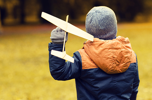 autumn, childhood, dream, leisure and people concept - happy little boy playing with wooden toy plane outdoors from back