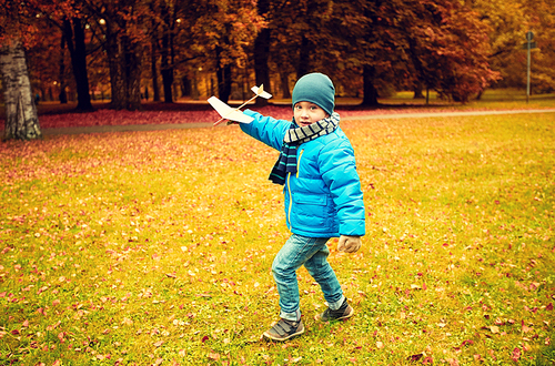 autumn, childhood, dream, leisure and people concept - happy little boy playing with wooden toy plane outdoors
