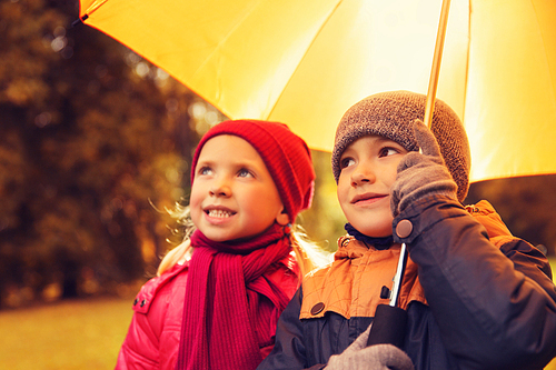 childhood, friendship, season, weather and people concept - happy little boy and girl with umbrella in autumn park