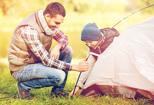 travel, tourism, hike and family concept - happy father and son setting up tent outdoors
