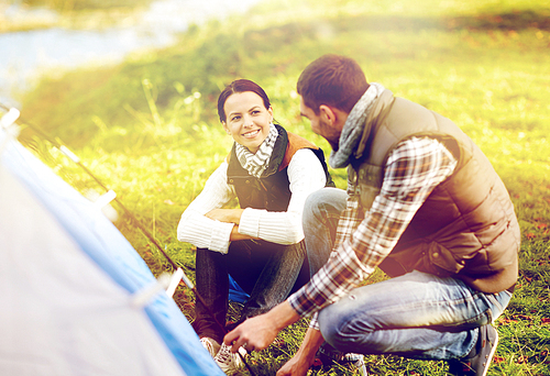 travel, tourism and hike concept - happy couple setting up tent outdoors