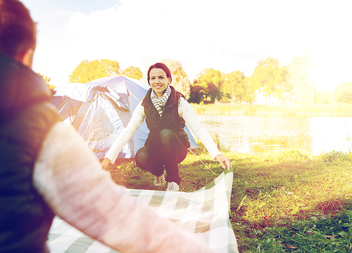 travel, tourism and hike concept - happy couple with picnic blanket at campsite
