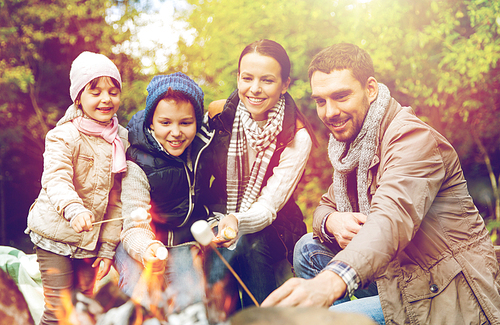 hike, travel, tourism and people concept - happy family roasting marshmallow over campfire