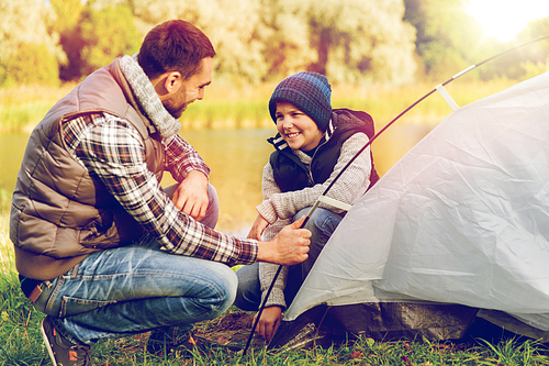 tourism, travel and hike concept - happy father and son hiking and setting up tent outdoors