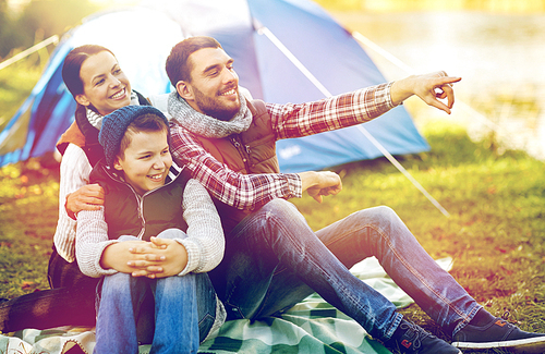 hike, travel, tourism and people concept - happy family over tent at camp site pointing finger to something