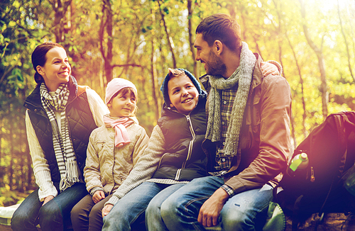 hike, travel, tourism and people concept - happy family sitting on bench and talking at camp in woods