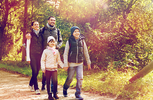 travel, tourism, hike and people concept - happy family walking with backpacks along road in woods