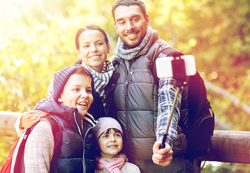 travel, tourism, hike, technology and people concept - happy family with backpacks taking picture by smartphone and selfie stick in woods